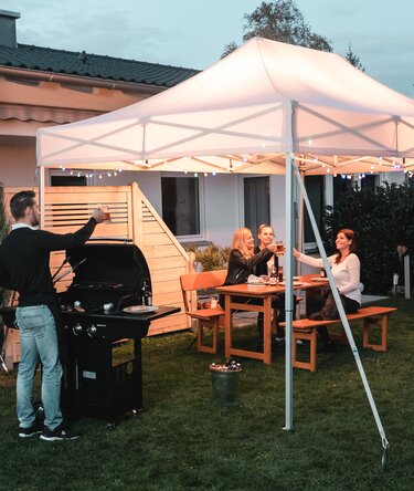 Friends celebrate a barbecue and garden party under the garden tent. The garden tent is festively decorated with fairy lights.