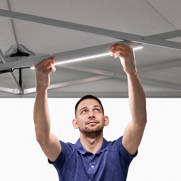 The man attaches the LED strips to the folding gazebo.