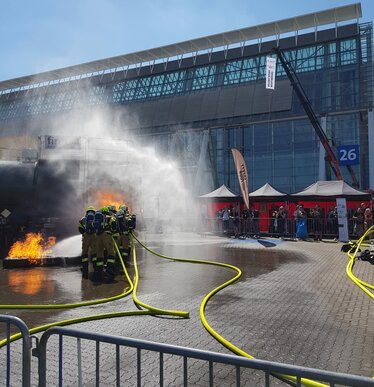 Trzy czarne pawilony 3x3 m z czerwonymi bocznymi p_achtami Ecotent na targach stra_y po_arnej Interschutz w Niemczech podczas symulacji sytuacji awaryjnej.